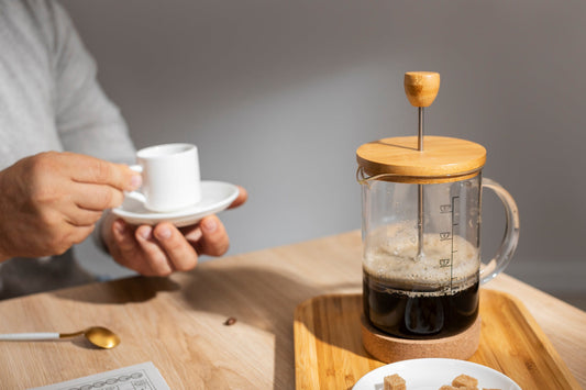 A man’s hands holding a cup of coffee with a french press sotting off to the side of the table.