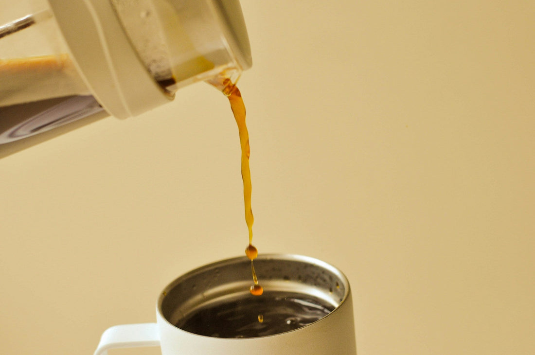Coffee being poured from a container into a travel mug.